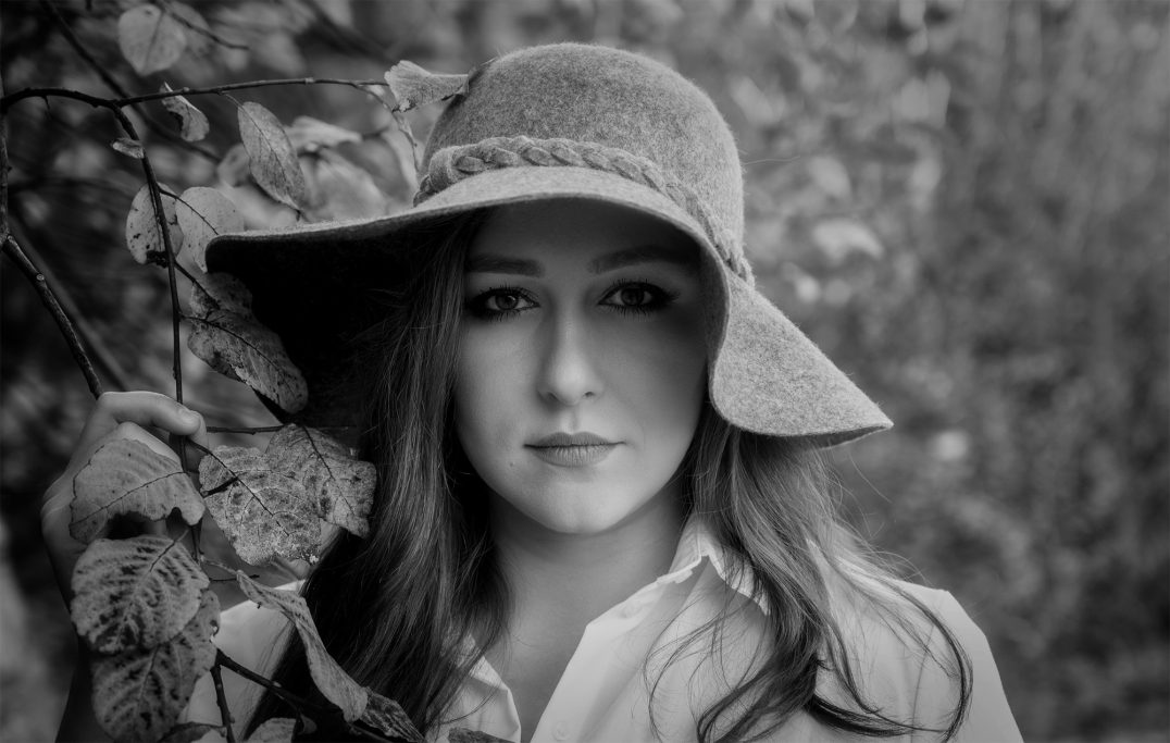 Junge Frau mit einem breiten Sonnenhut, umgeben von Pflanzen, in Schwarz-Weiß.