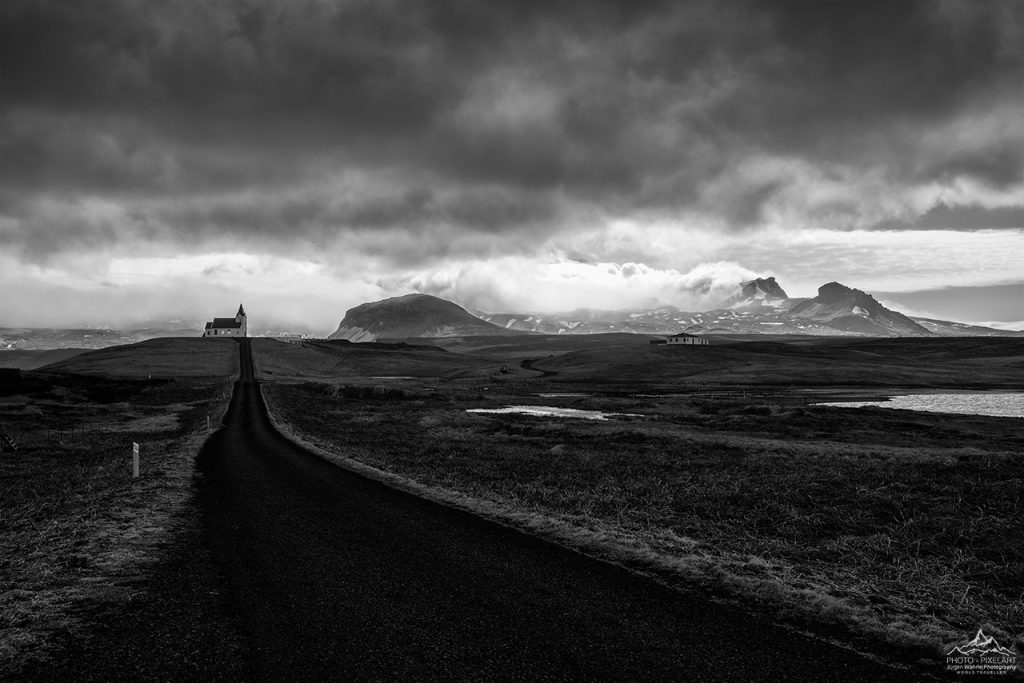 Schwarze und weiße Landschaft mit einer Straße, Bergen und dramatischem Himmel.