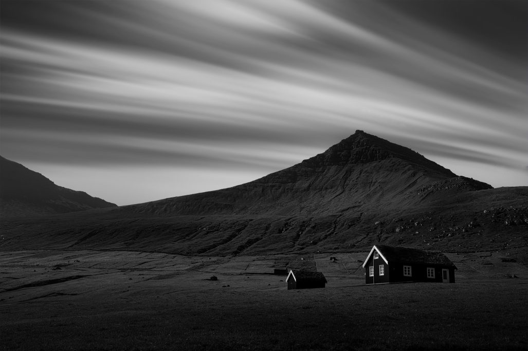 Schwarz-weiß Landschaft mit einem einsamen Haus und einem Berg im Hintergrund.