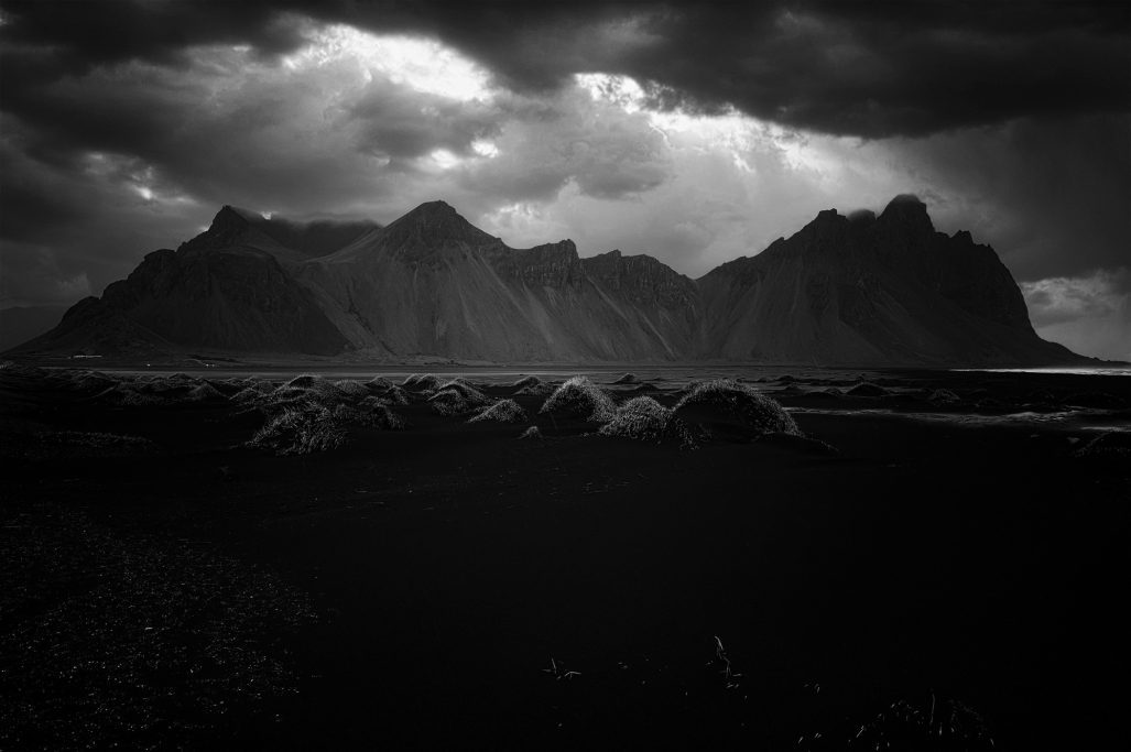 Dramatische Landschaft mit dunklen Bergen und wolkenverhangenem Himmel.