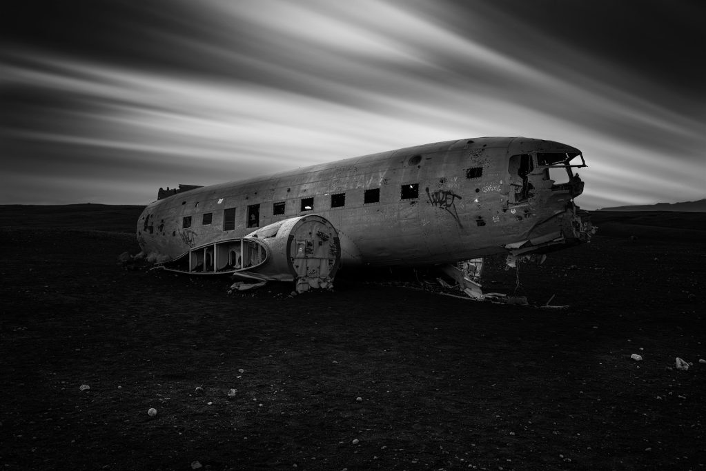 Verwittertes Flugzeugwrack in einer kargen Landschaft, schwarz-weiß fotografiert.