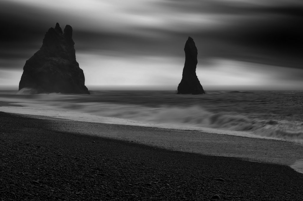 Dramatische Küstenlandschaft mit hohen Felsen und sanften Wellen im Vordergrund.